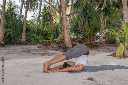 an adult female yoga instructor with a perfect figure does asanas in the fresh air in the shade of palm trees. The concept of fitness, sports and a healthy lifestyle