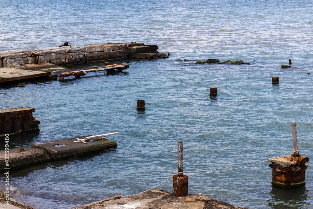 An ancient ruined boat dock. Wooden planks and pillars sticking out of the water at the ruined pier.