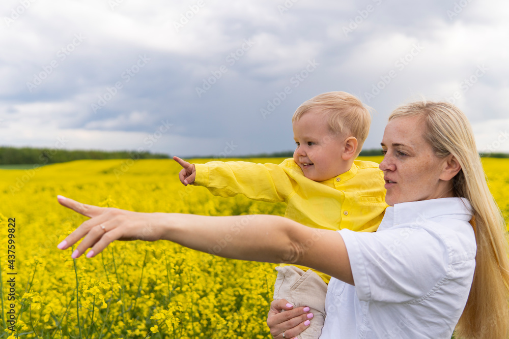 mom and son with blond hair on the field of yellow flowers point into the distance mom and son with blond hair on the field of yellow flowers point into the distance