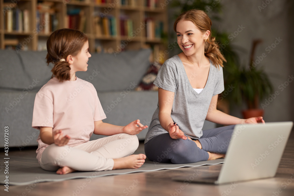 Healthy family mom and daughter meditating together at home while having online yoga class on laptop