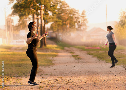 Fototapeta Naklejka Na Ścianę i Meble -  Young women exercising outdoors at sunset. Fitness outside. Outdoor activities with skipping rope.  Healthy active lifestyle.