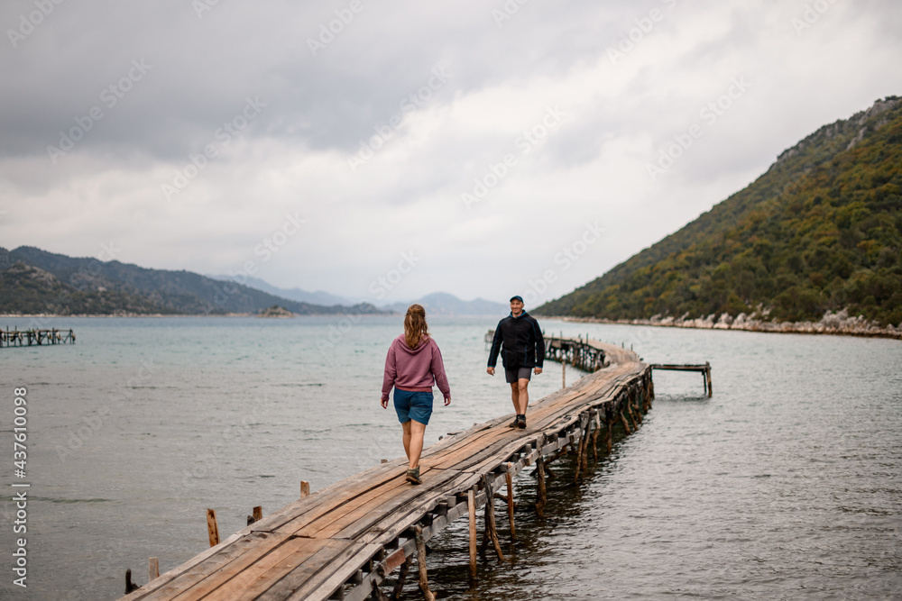 man and woman are walking on wooden pier against the backdrop of beautiful landscape