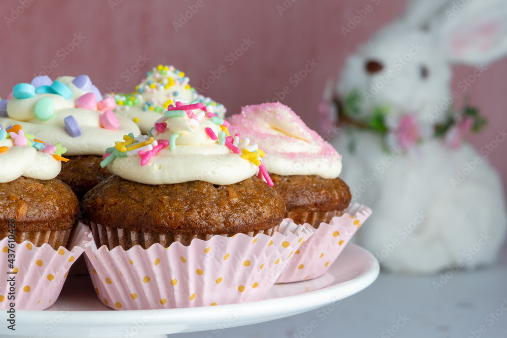 Carrot Cake Cupcakes on a white platter with a stuffed Easter Bunny on the background. Carrot Cake Cupcakes on a white platter with a stuffed Easter Bunny on the background.