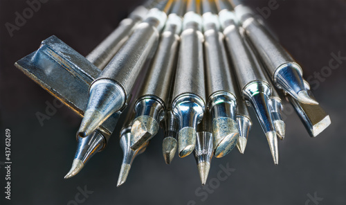 Set of soldering iron metal tips on a dark background. Various types, sizes and shapes of spiked replaceable heated tool bits for installation, repair or assembly work in electronics. Artistic detail.