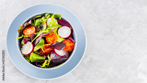 Healthy vegetable salad with cherry tomatoes, radish and mix salad. Vegan salad with mix of greens on gray background. Paleo diet concept. Copy space. Top view