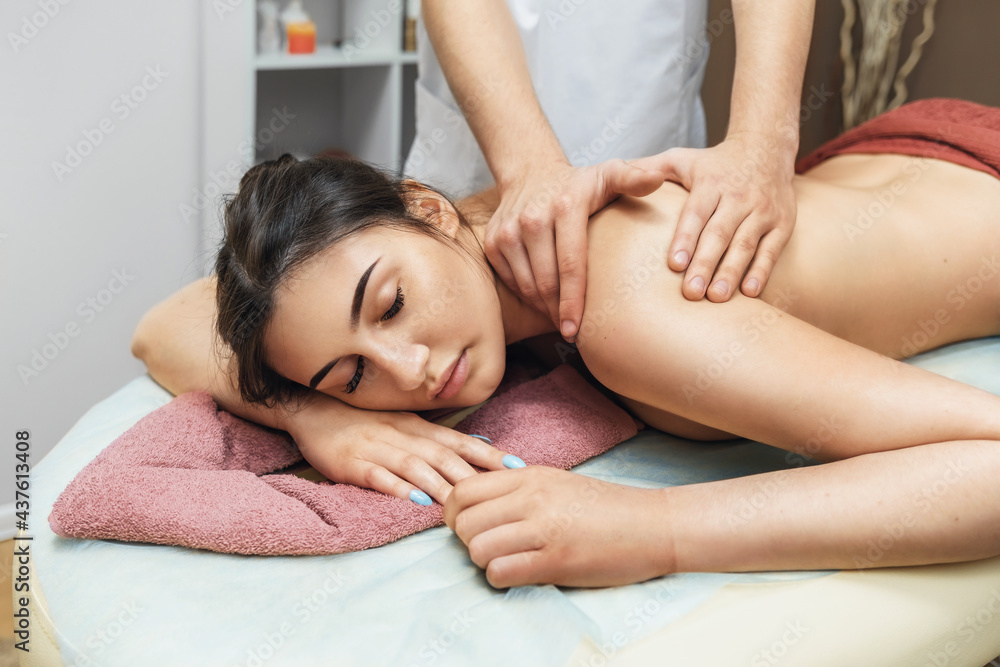 Young beautiful brunette woman in a spa salon is resting during a massage session in the trapezius muscles and cervical region Young beautiful brunette woman in a spa salon is resting during a massage session in the trapezius muscles and cervical region