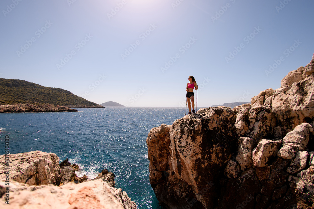view on woman standing on high rocky cliff against backdrop of seascape