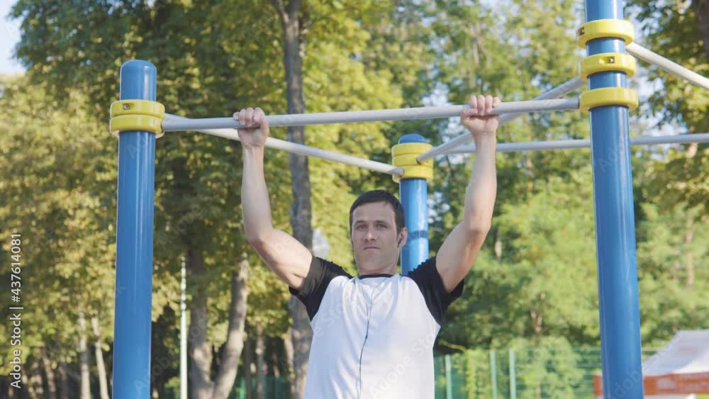 An attractive man pulls himself up on a horizontal bar on a bright sunny day.Sports with headphones. An attractive man pulls himself up on a horizontal bar on a bright sunny day.Sports with headphones.