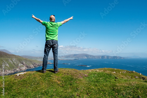 Bald male tourist standing on top of a mountain with spectacular view in the background. Moyteoge Head, Achill island, county Mayo, Ireland. Irish landscape. Sunny day, Travel concept