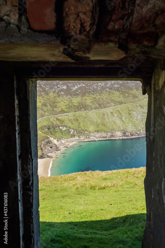 View on Keem beach from a door of an old building. Achill island  county Mayo  Ireland. Beautiful sandy beach with clear blue water. Bright nature landscape framed by dark building