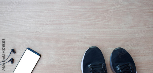 Sports shoes with smartphone and headphones on wooden table