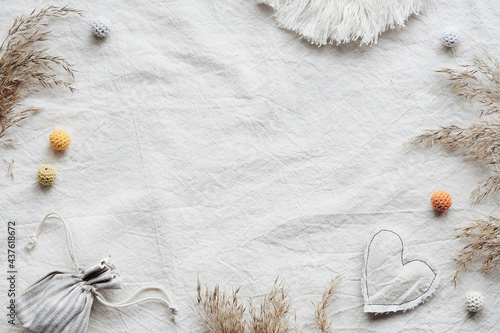 Textile flat lay with dry reeds, pampas grass and macrame. Bag with fragrant herbs, soft cotton heart. Off white tablecloth background with knitted cotton balls. Simple minimal flat lay, natural light photo