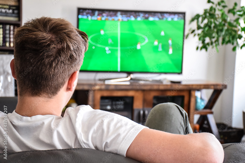 Young man watching soccer game on TV sitting on a couch at home Young man watching soccer game on TV sitting on a couch at home