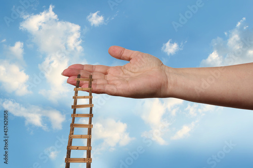 female hand outstretched against beautiful summer landscape, blue sky with clouds, wooden staircase in palm, concept of transcendence, infinity, height, the kingdom of God