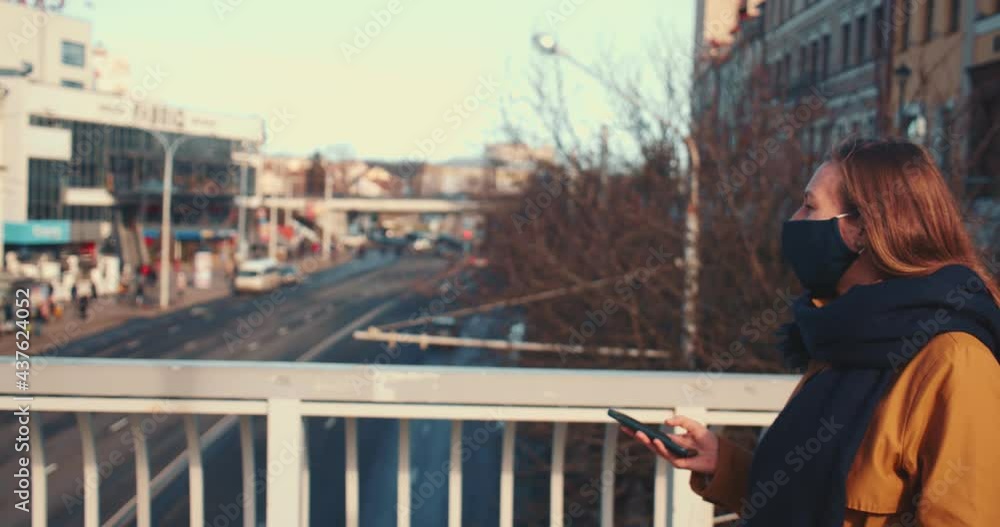 Side view happy attractive woman in face mask using smart phone app walking along sunny city street bridge background. Side view happy attractive woman in face mask using smart phone app walking along sunny city street bridge background.