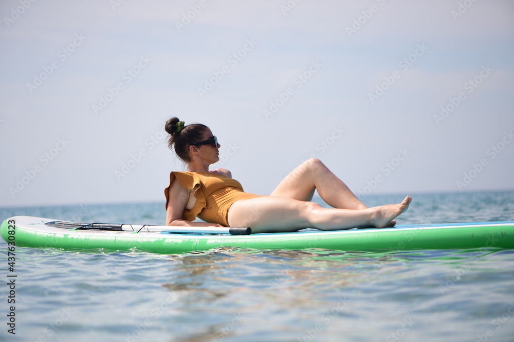 a woman in a yellow swimsuit and sunglasses rests on the sup in the Black Sea. Hot and sunny summer