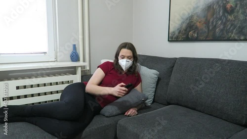 Attractive woman watching TV changing the channel wearing a white face mask