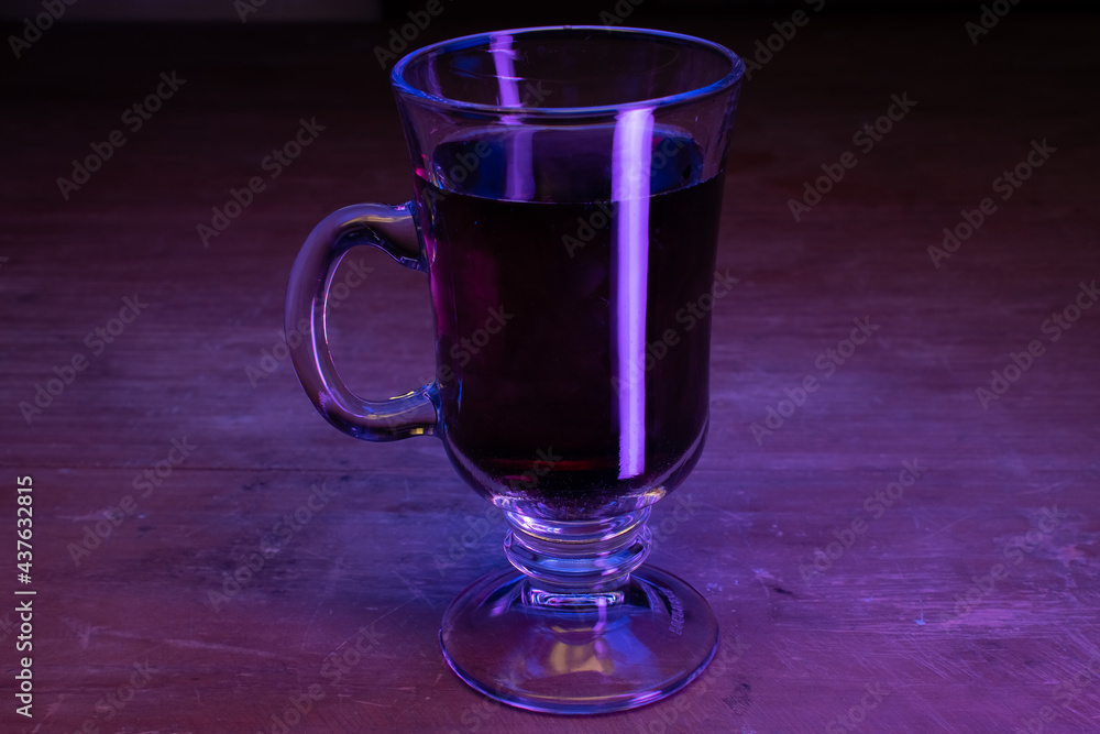 Cappuccino glass cup with dark liquid and neon uv lights on a wooden table Cappuccino glass cup with dark liquid and neon uv lights on a wooden table