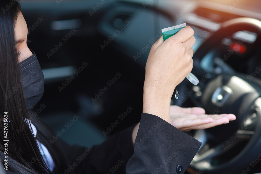 Naklejka premium Rear view asian woman hands in business black suit with protect mask for healthcare use alcohol gel hand sanitiser for hygiene in automobile and driving car. New normal and social distancing concept