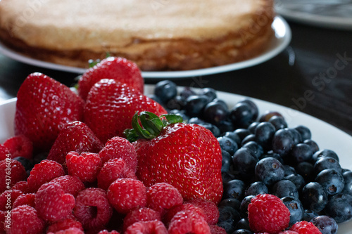 Plate of fresh juicy strawberries and blueberries with stack of pancakes in the back. Summer breakfast.