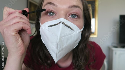 Pretty girl putting mascara/makeup on while wearing a white face mask