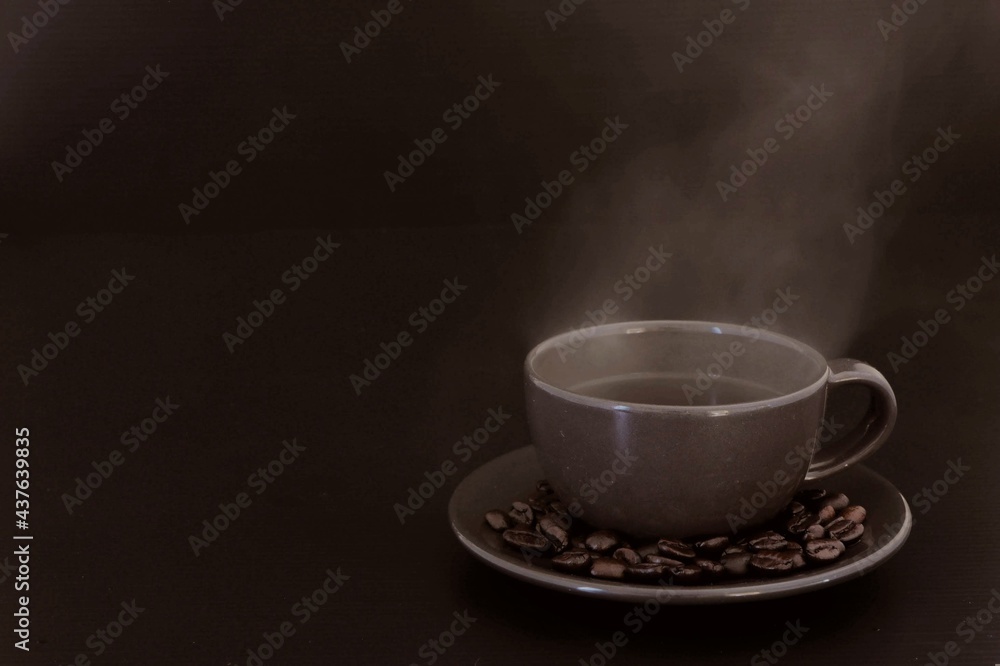 Obraz premium cup of coffee with beans, aroma​, hot​ steam​ from​ black​ coffee​ on​ dark​ and​ blur​ scene​