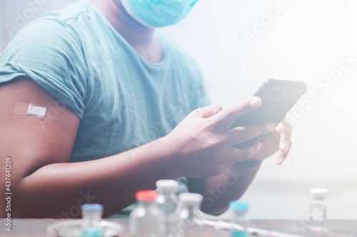 Youngman wearing a protective mask Show plaster on the shoulder Use your smartphone to find information about the impact of post-vaccination against covid-19  health care guidelines  health protection