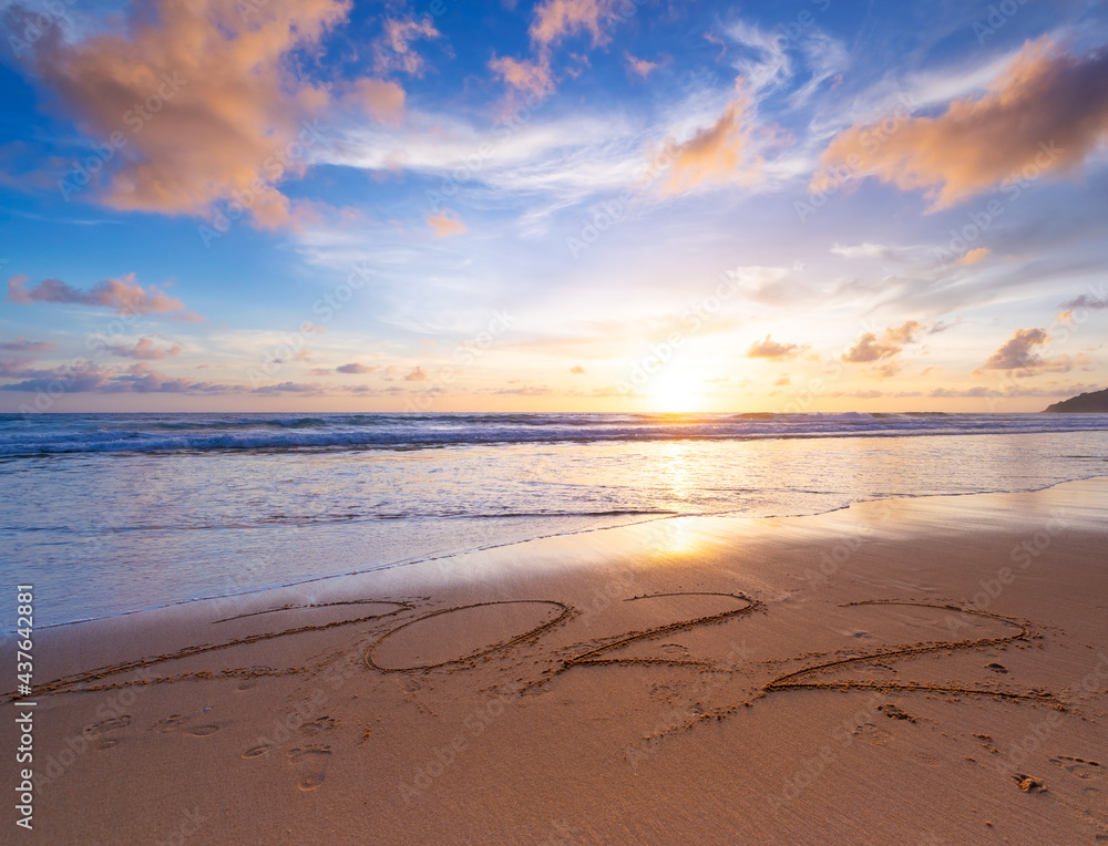 Happy New Year 2022, Lettering on the beach with waves and sunset sky Numbers 2022 year on the seashore, Message hand written in the golden sand on beautiful sunset or sunrise golden sky background.