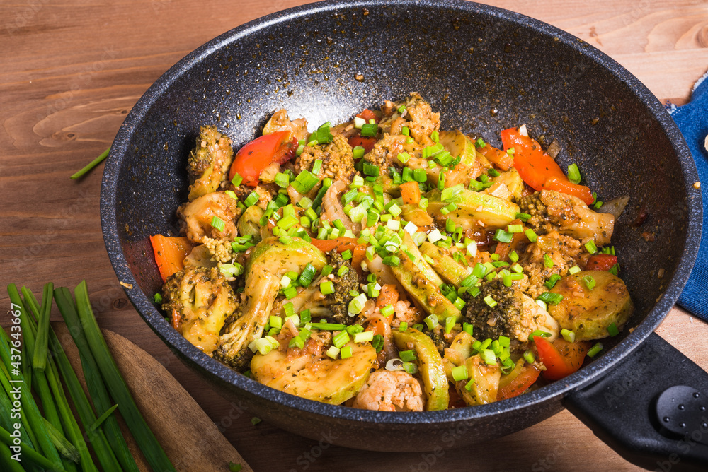 Fried, stewed, cooked, fresh vegetables in a modern wok, sprinkled with chopped spring onions, on a wooden table, close-up - vegetarian healthy cuisine Fried, stewed, cooked, fresh vegetables in a modern wok, sprinkled with chopped spring onions, on a wooden table, close-up - vegetarian healthy cuisine