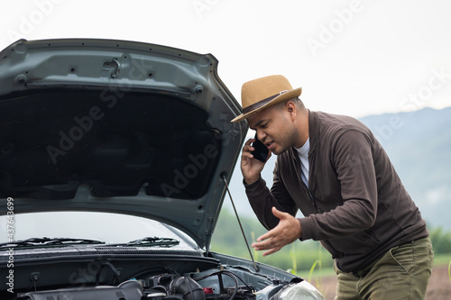 Asian man has broken down car on the road he talking on phone to call someone to help or mechanics car service. Emergency assistance service