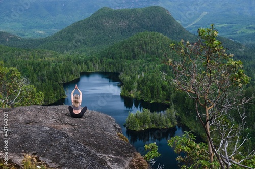 Woman meditating on rock above blue lake. Lily Lake in Madeira park near Sechelt. Sunshine Coast. British Columbia. Canada photo