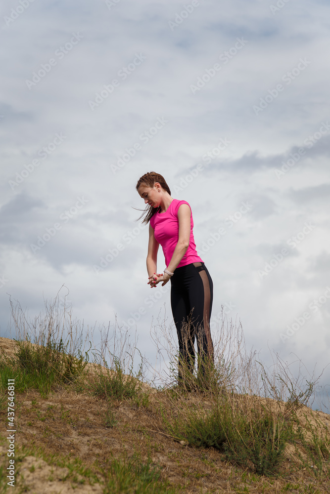 Young sporty woman in sportswear on hill top stretching or warming up on cloudy sky background. Fitness, healthy way of life, wellbeing, freedom, loosing weight concept. Young sporty woman in sportswear on hill top stretching or warming up on cloudy sky background. Fitness, healthy way of life, wellbeing, freedom, loosing weight concept.