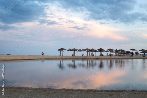 A sparsely populated beach with straw umbrellas at the end of the swimming season on the south coast.