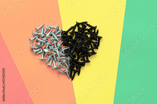 Heart of two opposite halves on a rainbow background, Valentine's card made of screws on colored paper, black and gray hardware as a brutal declaration of love