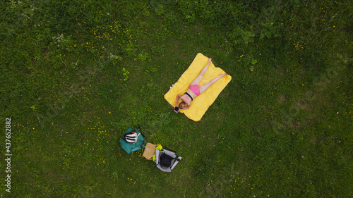 Woman sunbathes on a green meadow. Lying on his stomach, on a yellow rug. Aerial photography.