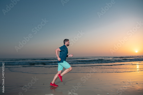 Male model in sportswear exercising outdoors on beach. Athletic young man running, fitness model on sea sunset or sunrise.