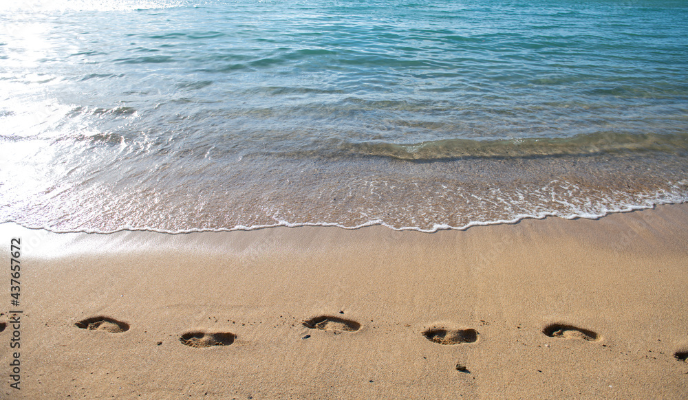 Fototapeta premium Beach background footprints in sand foot print. Concept for travel vacation. Footsteps in sand on summer tropical getaway holidays vacation with blue ocean.