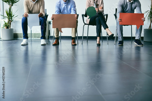 Unrecognizable business people holding speech bubbles while sitting in a row in waiting room