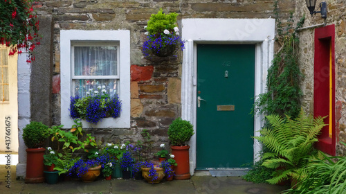 Picturesque facade of a traditional stone house with ornate colored green door and white window. With many pots and flowers in front. kirkwall, scotland