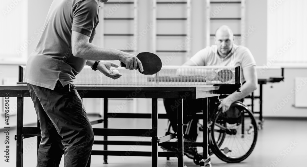 Adult disabled man in a wheelchair play at table tennis with his coach Adult disabled man in a wheelchair play at table tennis with his coach