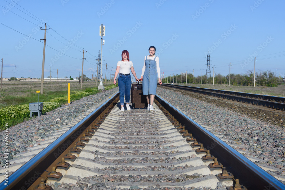 Two young women walk along the railroad tracks with large suitcase. Travel concept