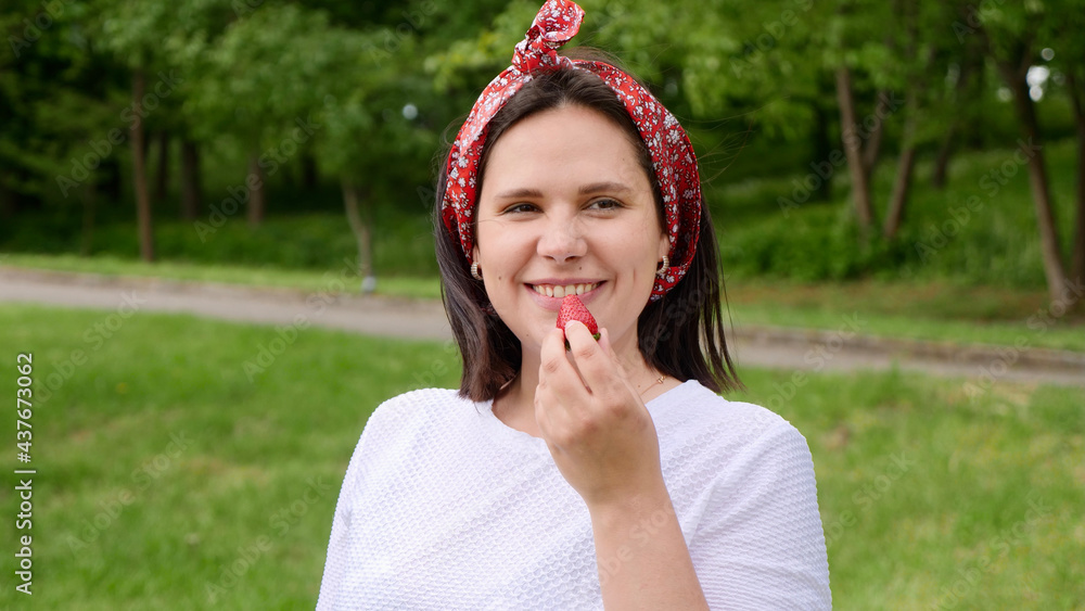 Girl eating strawberry, smiling happy, looking at camera. Young woman eating red strawberry berry. Portrait of mom, housewives, farmer Girl eating strawberry, smiling happy, looking at camera. Young woman eating red strawberry berry. Portrait of mom, housewives, farmer