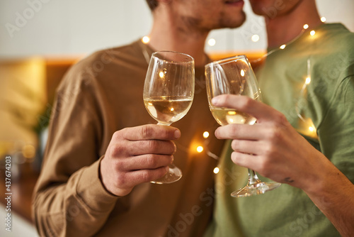 Same-sex male partners kissing while holding wine glasses