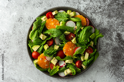 Delicious healthy salad of spinach leaves, tangerine and avocado slices, tomato and radish with seeds, salad in a plate close-up ,top view, copy space