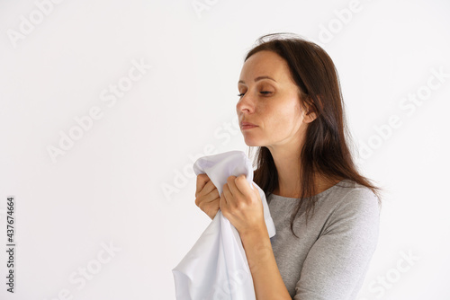 A cute Caucasian woman holding a clean white scent shirt on a light background. The concept of home care for clothing