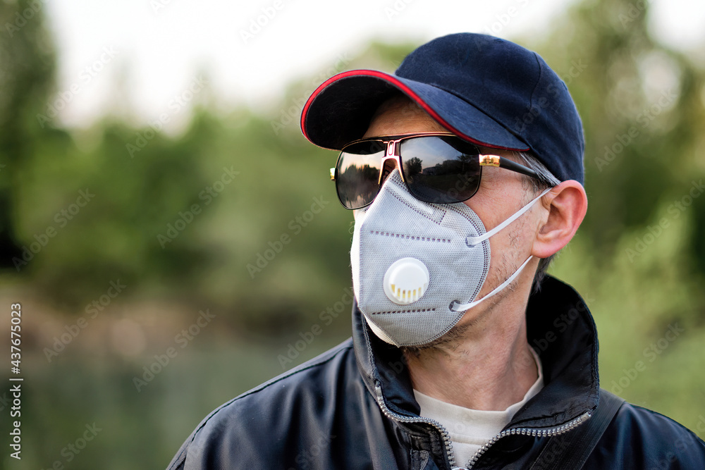 A man wearing respirator mask, sun glasses and a cap outdoors. Stock Photo  | Adobe Stock