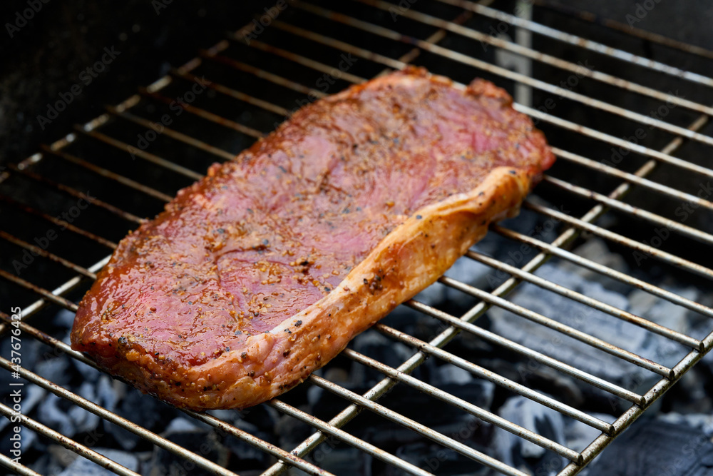 1 raw steak (rump steak) of beef lies on a stainless steel grill grate. Glowing coals roast the delicacy. View from diagonally in front. 1 raw steak (rump steak) of beef lies on a stainless steel grill grate. Glowing coals roast the delicacy. View from diagonally in front.