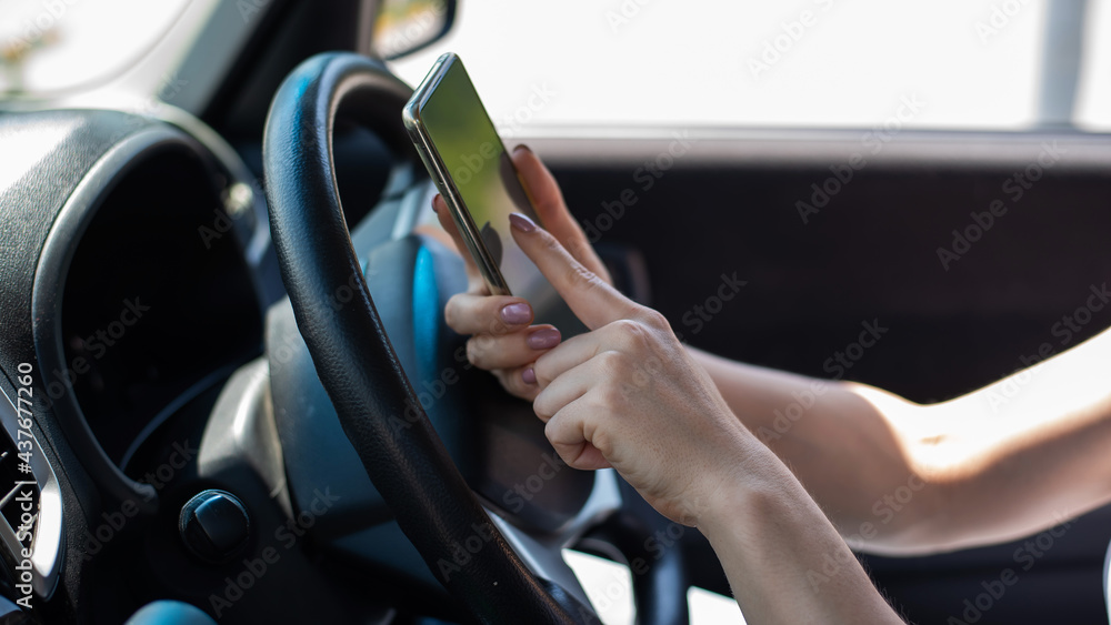 A faceless woman uses a mobile phone while driving a car. The girl uses the navigation in the smartphone