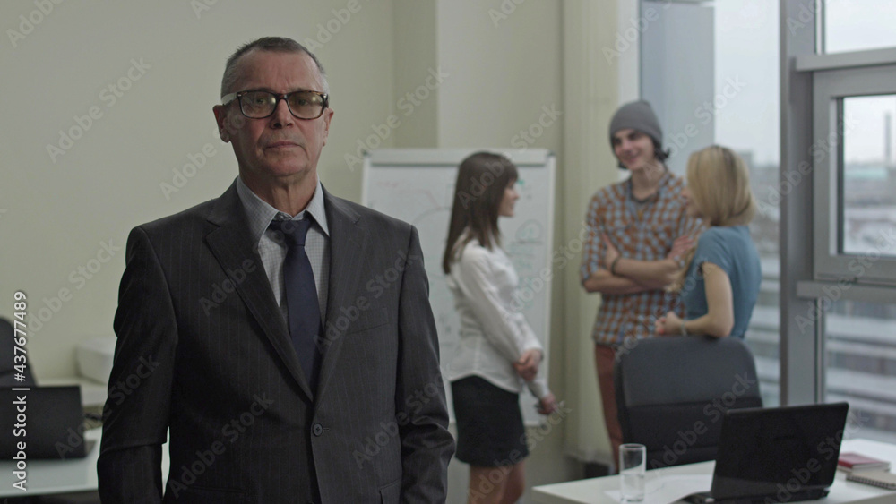 Portrait of serious older businessman who stands in front of coworkers Portrait of serious older businessman who stands in front of coworkers