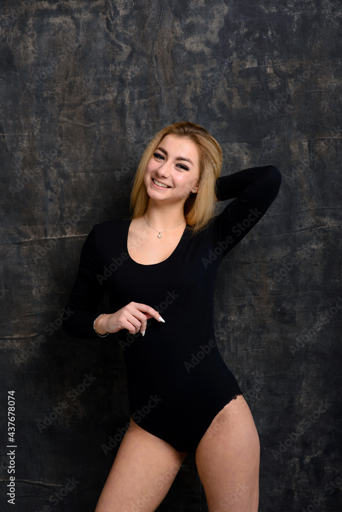 Young blonde plump woman with bright makeup in black bodysuit at dark background